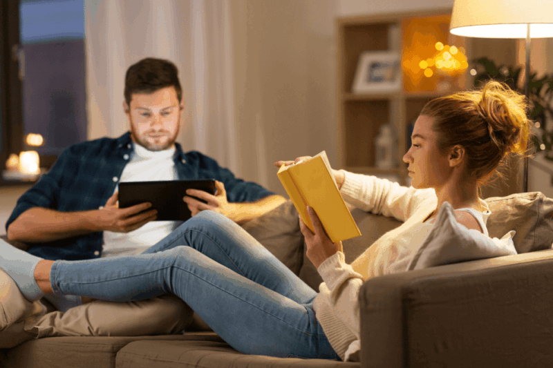 Par sidder i sofa og er optaget af hver deres aktivitet – kvinden læser, manden kigger på tablet. Der er afstand mellem dem