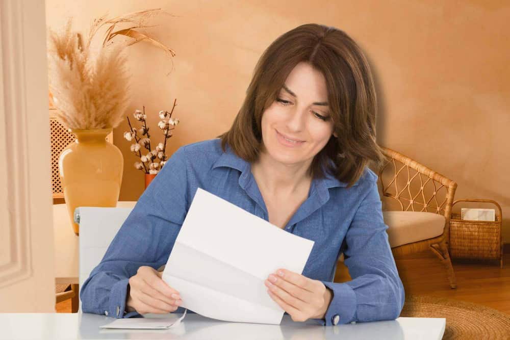 Kvinde i blå skjorte smiler, mens hun læser et brev – anerkendende ord som kærlighedssprog