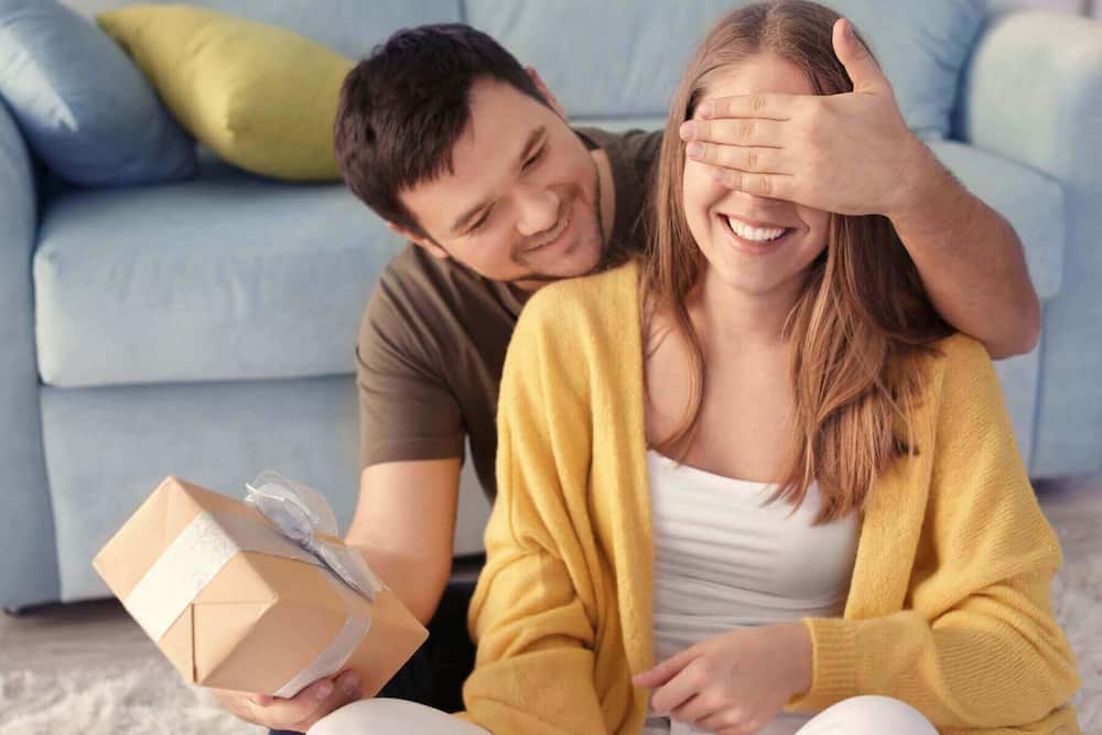 Mand overrasker kvinde med gave og hånd for øjnene – symbol på kærlighedssproget “gaver”